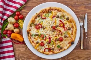 A full pizza on a plate with a knife, fork, and fresh vegetables next to it.